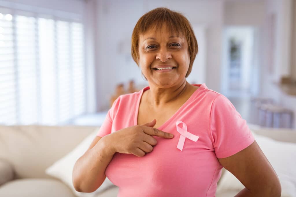 African american senior woman pointing at breast cancer awareness ribbon on pink t-shirt